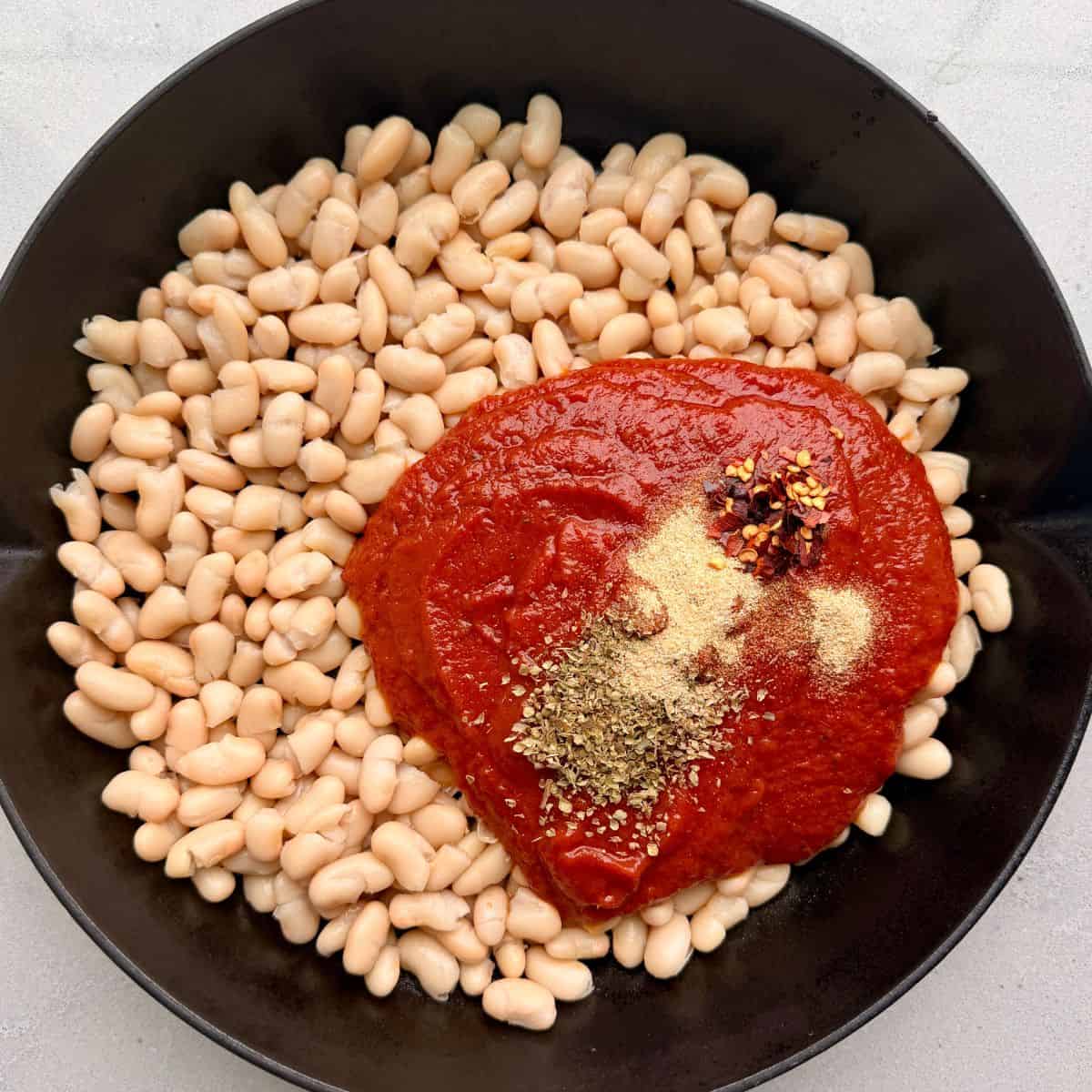 Marinara sauce and seasonings added on top of beans in a skillet before combining.