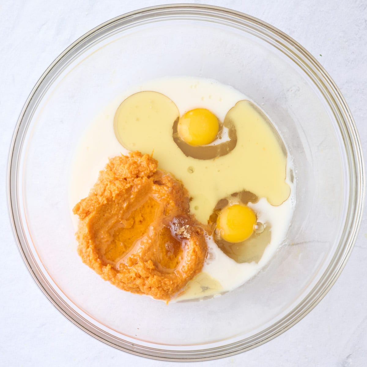 Mash sweet potatoes, eggs, milk, and oil in a bowl before mixing for the waffle recipe.