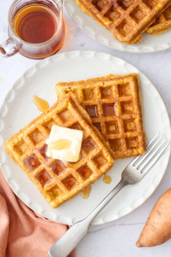 Stack of two fluffy sweet potato waffles on a plate with a pat of butter and syrup on top.