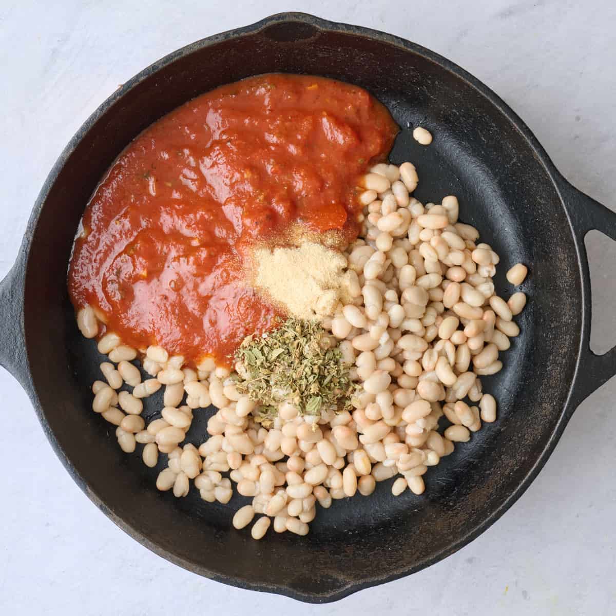 Drained beans in a 10-inch cast iron skillet with marinara, oregano and garlic powder before combining.
