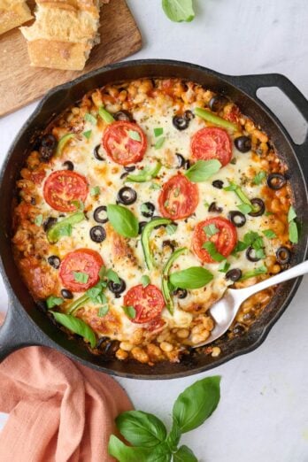 Pizza beans garnished with fresh basil with crusty bread nearby, serving removed with spoon dipped inside.