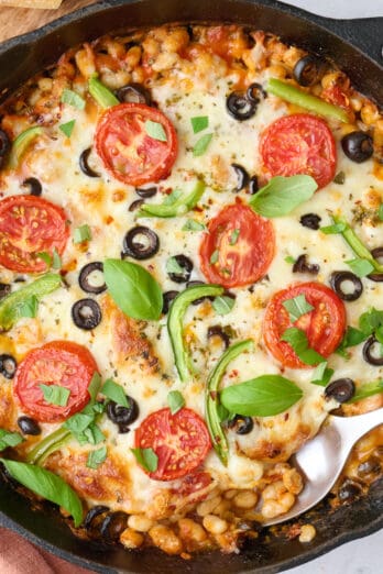 Pizza beans garnished with fresh basil with crusty bread nearby, serving removed with spoon dipped inside.