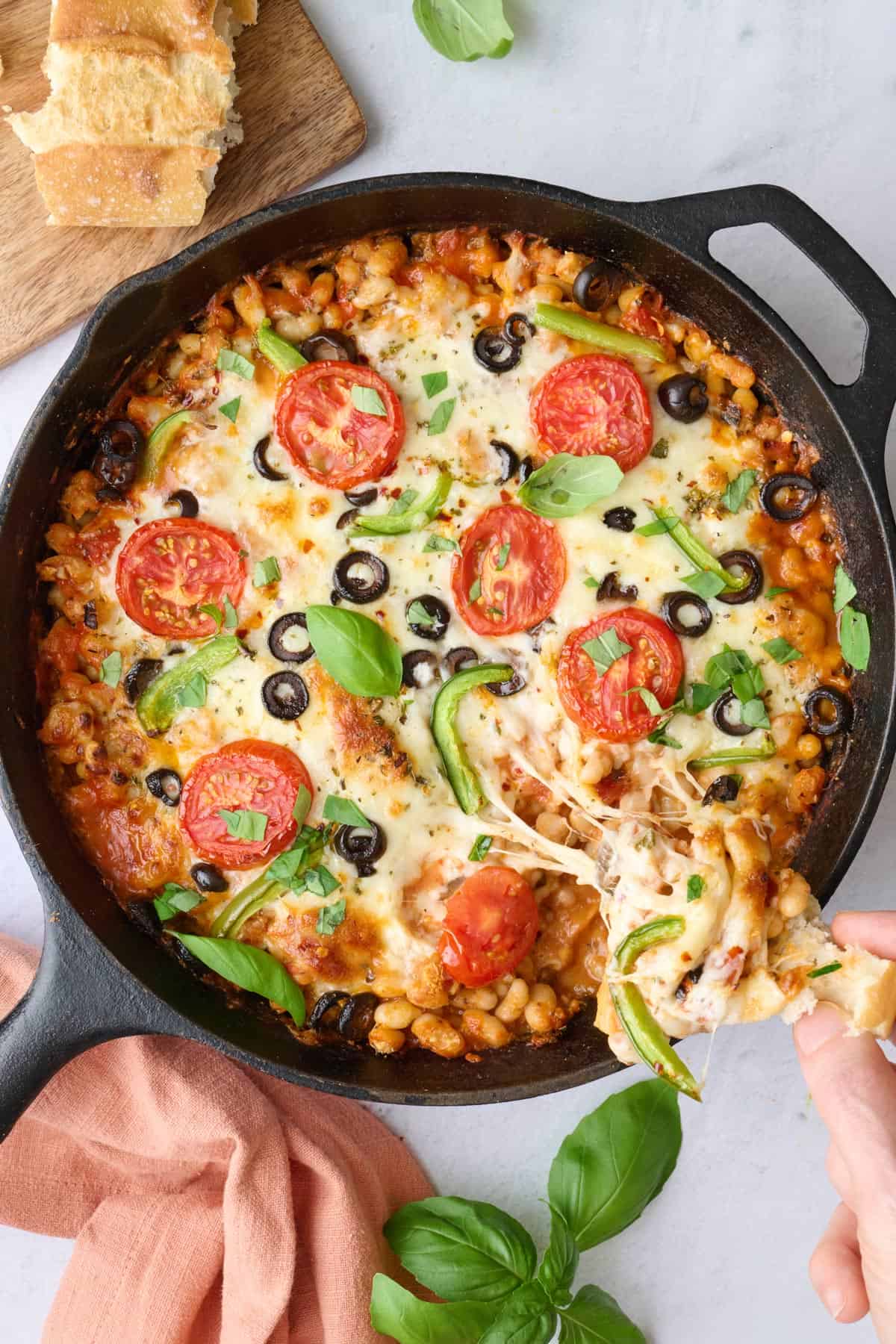Crusty bread with pizza beans on it being pulled from the skillet with a cheese pull.