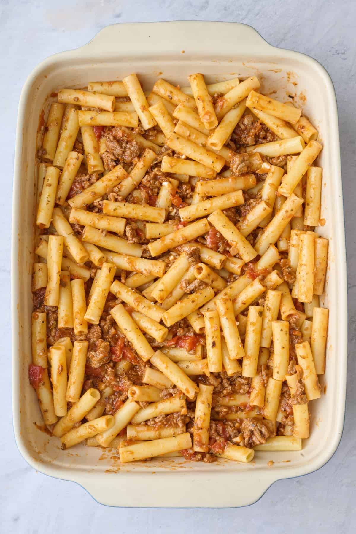 Half the cooked pasta in a baking dish with pasta sauce.