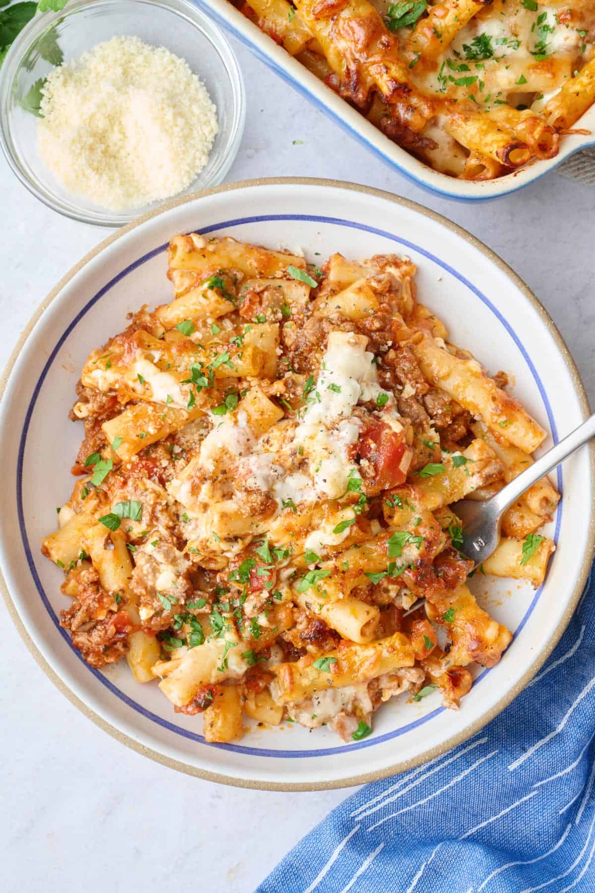 A serving of ziti in a shallow bowl with baking dish nearby.