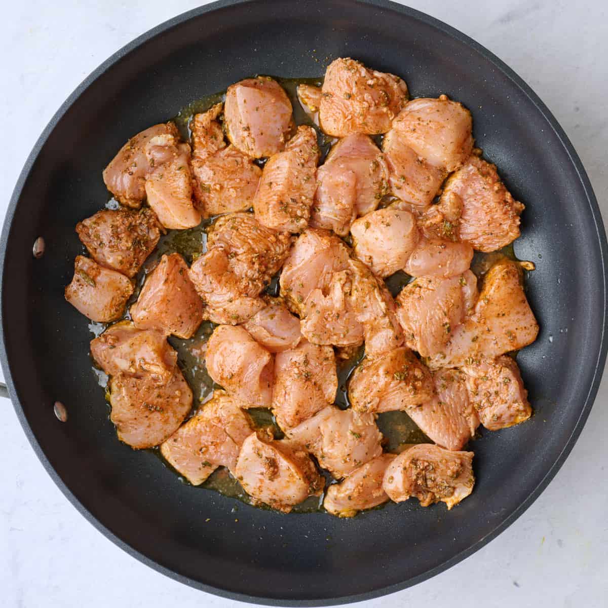 Marinated chicken in a large non stick skillet in a single layer.