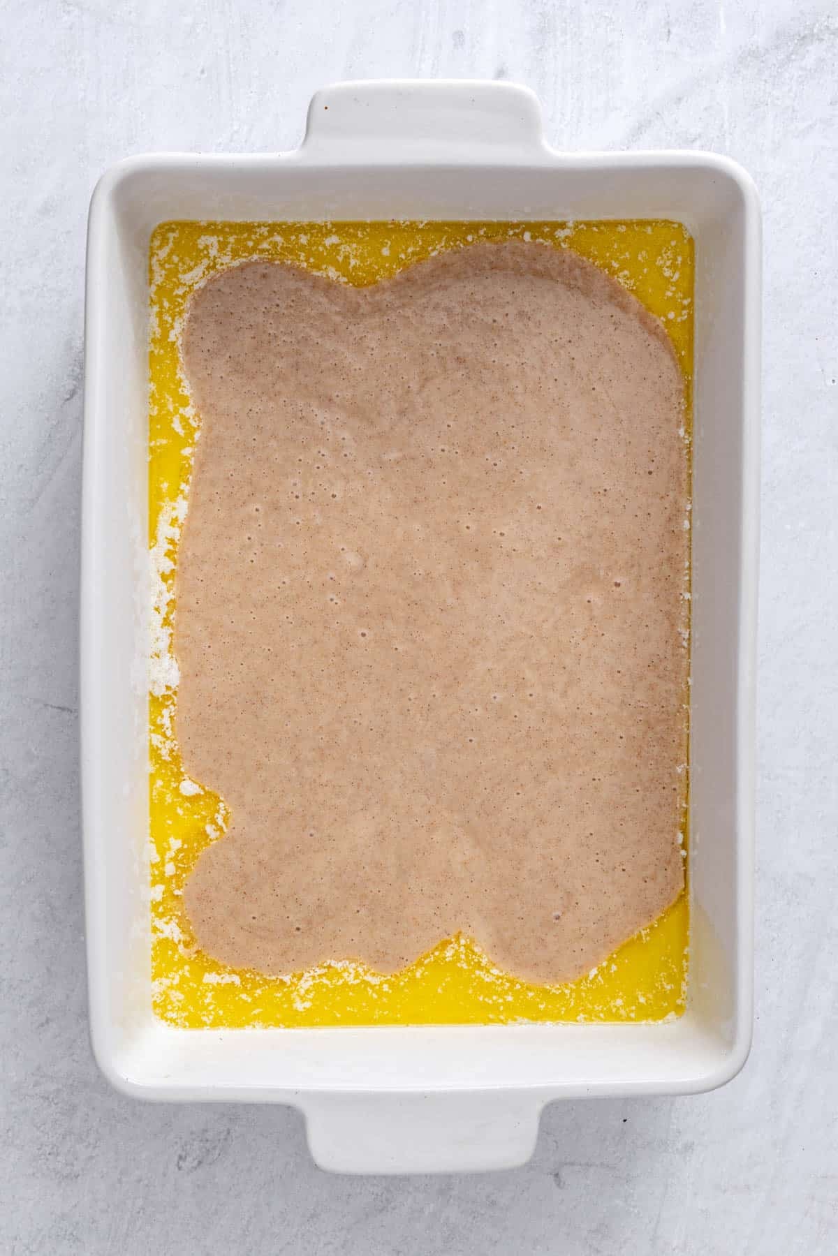 Melted butter in a 9x13 baking dish with batter poured on top.