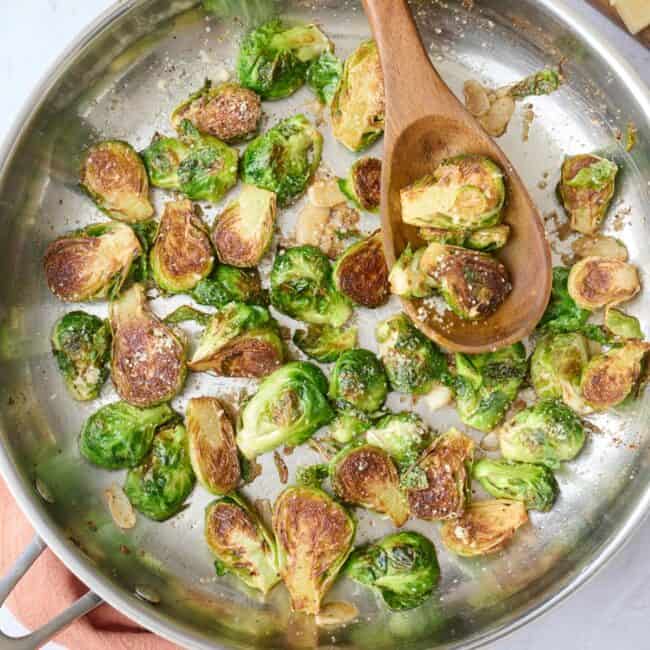 Sauteed brussel sprouts in the skillet garnished with parm, serving spoon dipped inside.