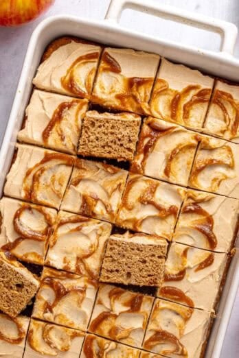 Applesauce cake in the baking dish topped with cream cheese frosting with apple butter swirl, cut into 24 pieces with a few pieces propped up to see inside.