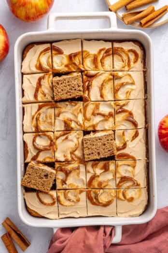 Applesauce cake in the baking dish topped with cream cheese frosting with apple butter swirl, cut into 24 pieces with a few pieces propped up to see inside.