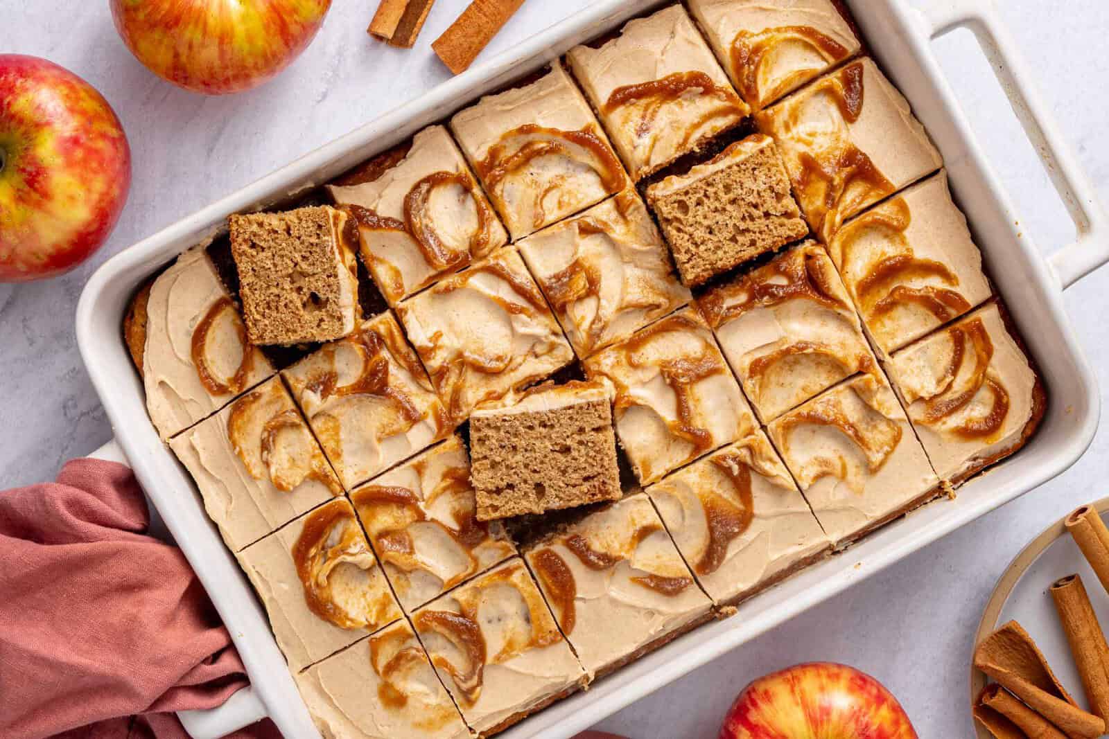 Applesauce cake in the baking dish topped with cream cheese frosting with apple butter swirl, cut into 24 pieces with a few pieces propped up to see inside.