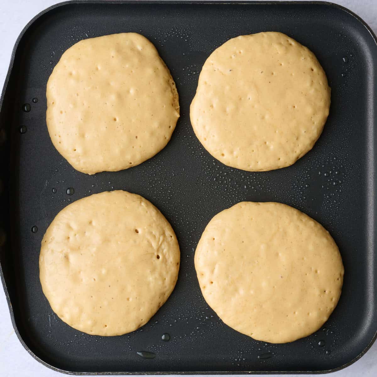 Four pancakes scooped on a square pan.