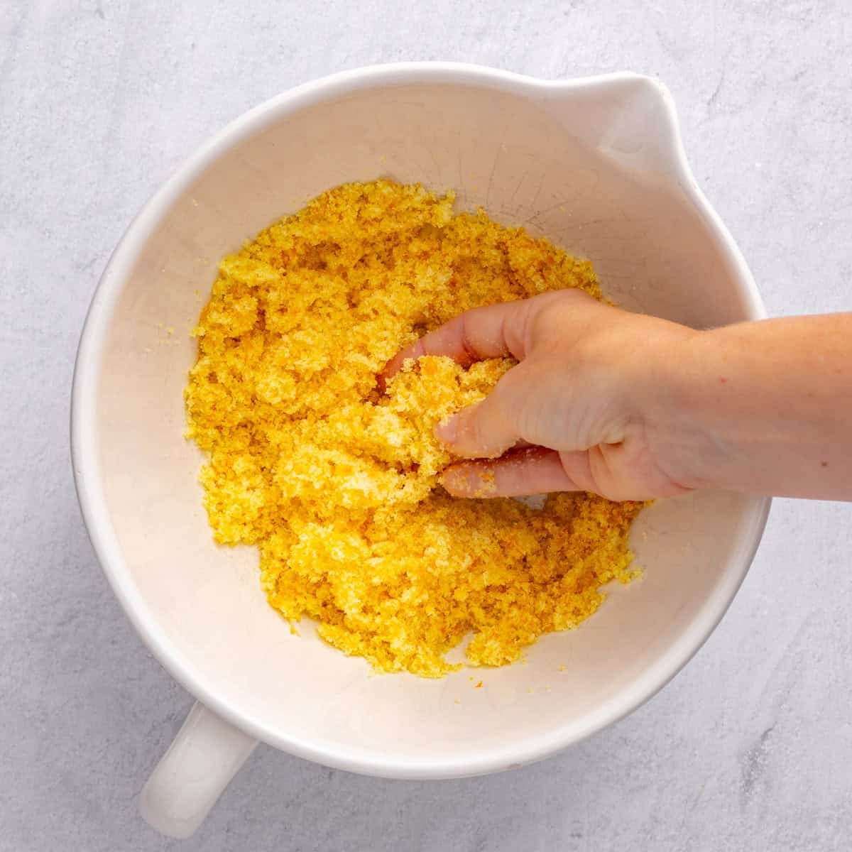 Sugar and orange zest in a large bowl with fingers rubbing together.